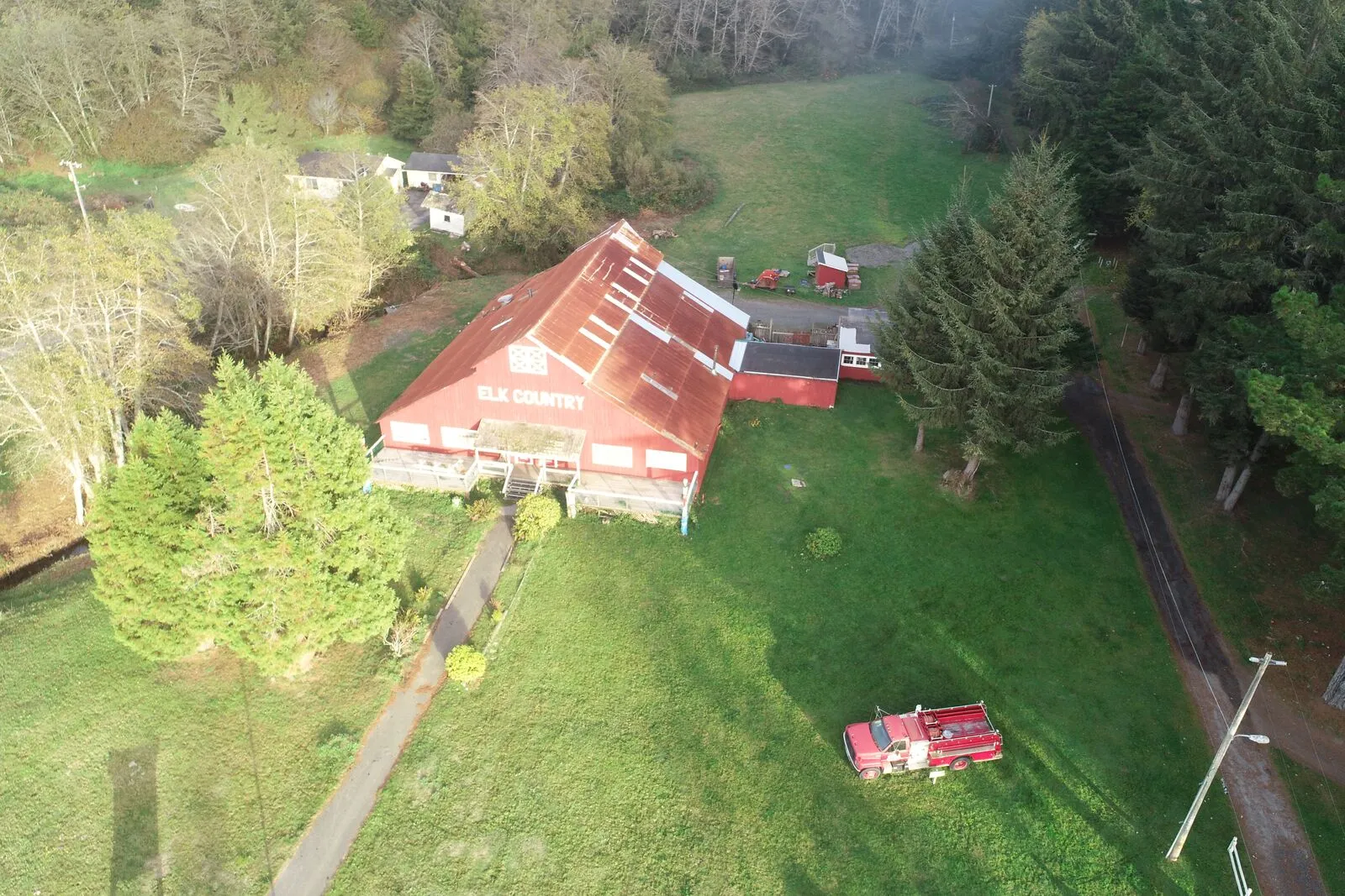 Aerial photo of the resort’s large red barn, with “ELK COUNTRY” painted on its roof, surrounded by lawn, conifers and outbuildings, with an old red fire truck parked on the grass.