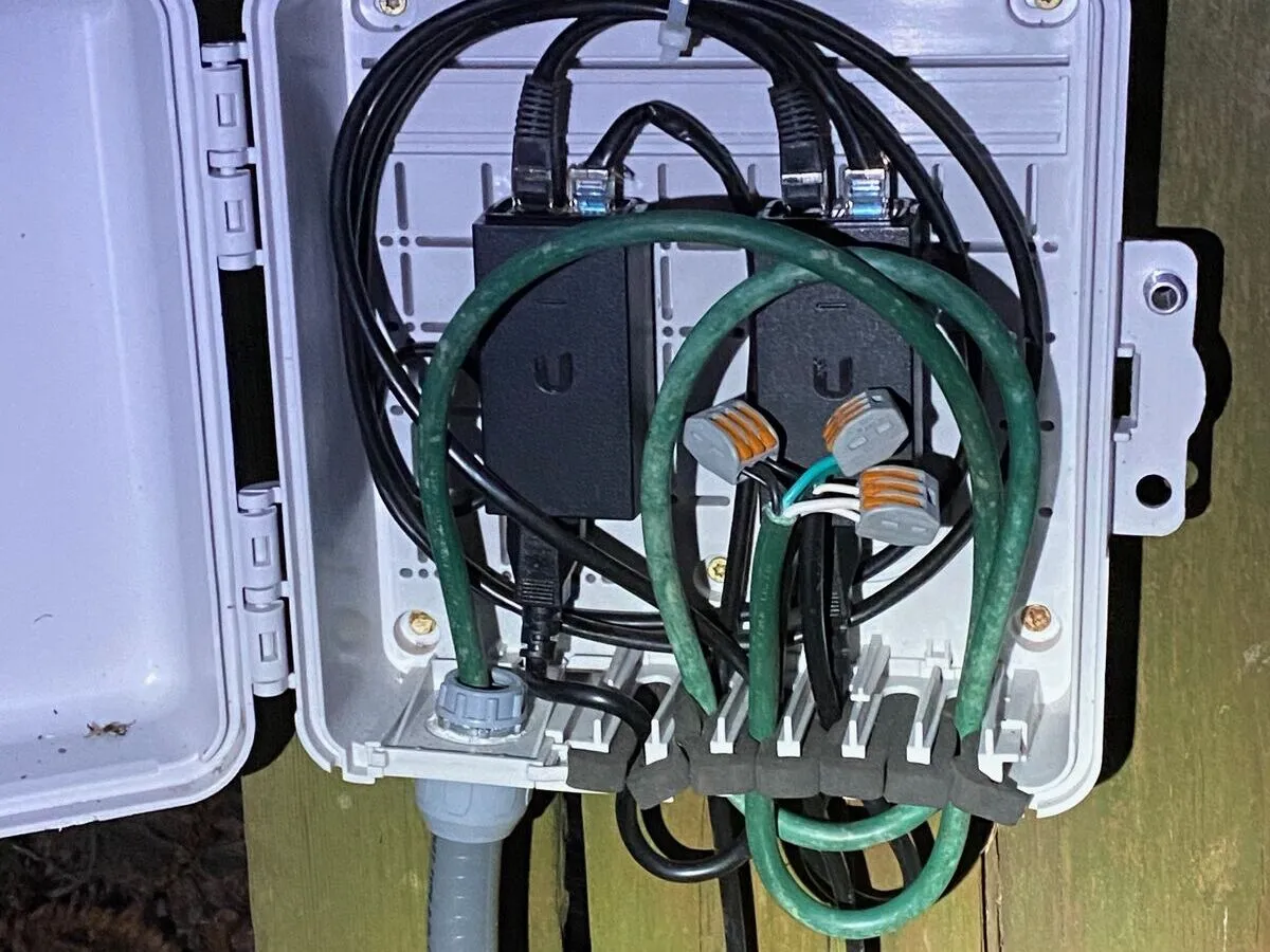 A weatherproof enclosure mounted on a wooden post, open to show neatly dressed cables and connectors, with flexible conduit entering from below.