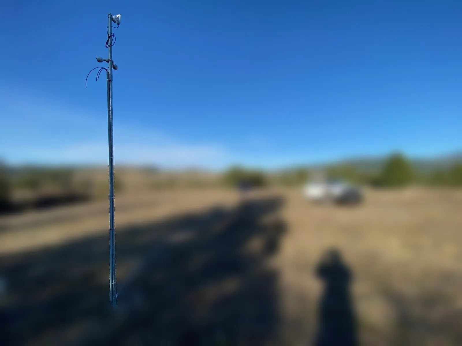 Solar-powered camera pole in sharp focus against a blurred dry field and blue sky
